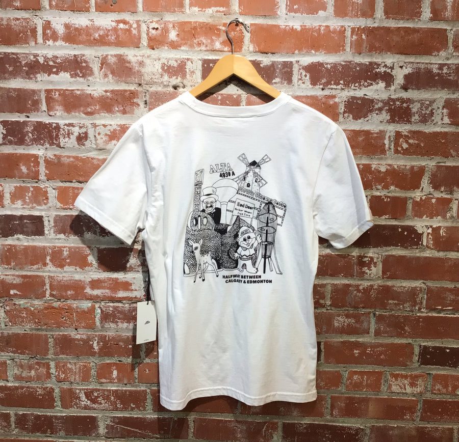 The white Alta Locals Only tee hanging on the shop's brick wall, Red Deer legends printed on the back